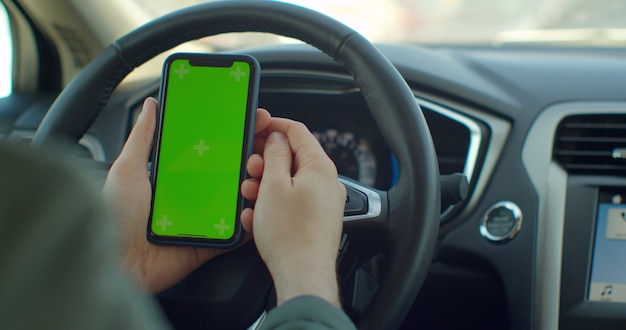 Man mano che tiene uno smartphone con schermo vuoto verde nell'auto elettrica per la direzione
