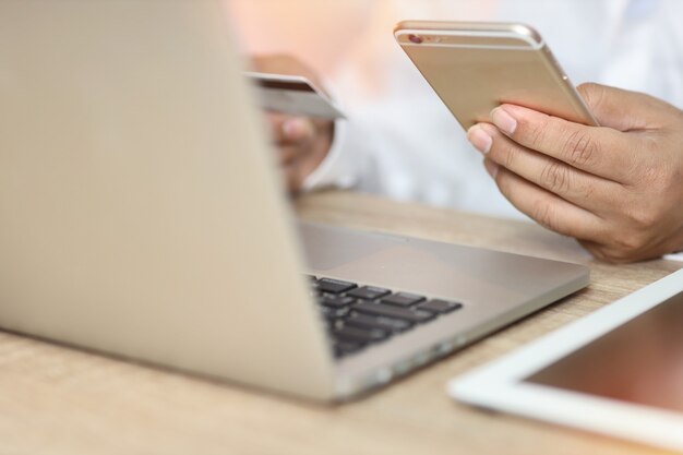 Man mano in camicia bianca seduto e tenendo la carta di credito e utilizzando il computer portatile sul tavolo