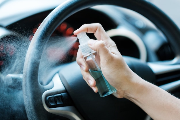 Man mano spruzzo disinfettante con alcool sul volante nella sua auto. ntisettico, concetto di igiene e sanità