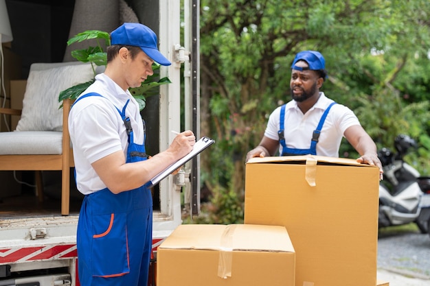 Man Mover in uniforme blu controlla le liste sugli appunti mentre scarica le scatole di cartone dal camion