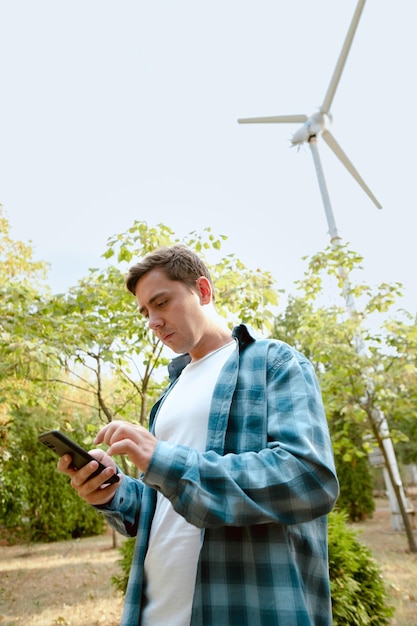 Man taking notes on wind turbine performance standing in a park with a windmill in the background