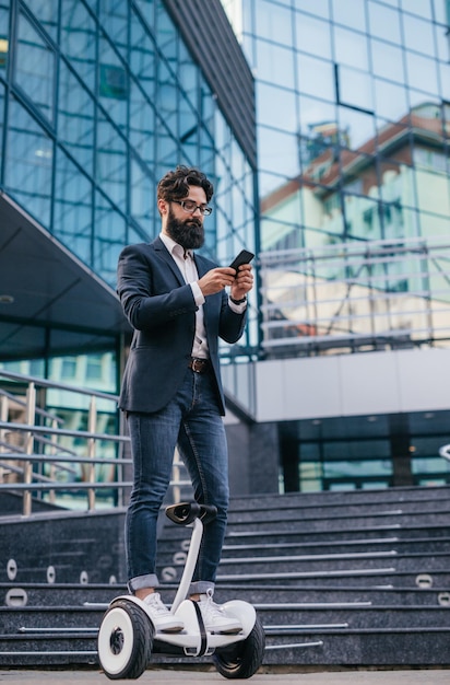 Manager barbuto che utilizza lo smartphone su hoverboard