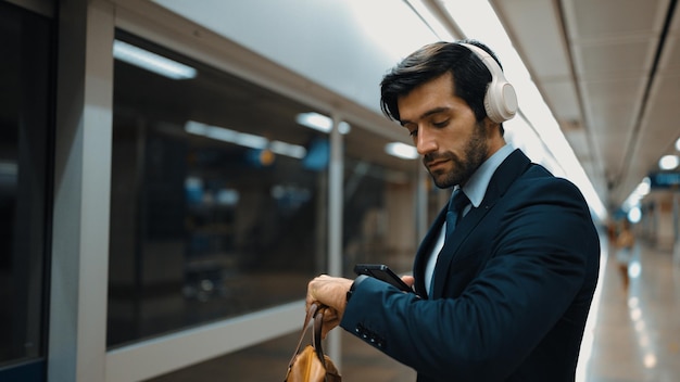 Manager che indossa le cuffie alla stazione ferroviaria mentre tiene in mano un telefono cellulare esultante