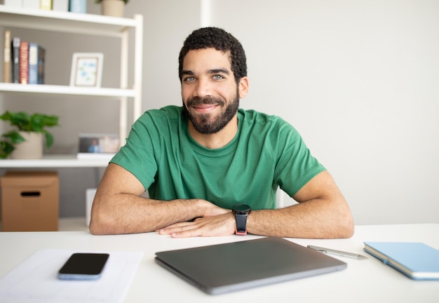 Manager di ragazzo arabo millenario sorridente con la barba sul posto di lavoro con smartphone con schermo vuoto