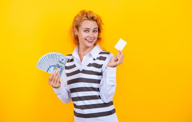 Manager donna sbalordita tenere contanti dollari denaro contro carta di credito isolato su giallo