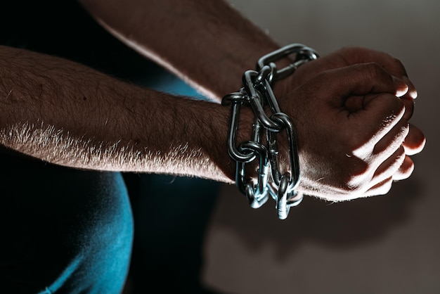 Manca incatenata seduto uomo caucasico prigioniero concetto di pena detentiva per i trasgressori tratta di esseri umani violenza contro gli uomini donne schiavo uomo tono grigio scuro