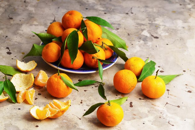 Mandarini (arance, mandarini, clementine, agrumi) con foglie in lastra blu su fondo grigio cemento. Cibo vegetariano biologico. Frutti locali invernali. Concetto di mangiare sano detox.