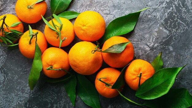 Mandarini (arance, mandarini, clementine, agrumi) con foglie su fondo grigio cemento. Agrumi dall'albero. Alimento vegetariano biologico. Frutti locali invernali. Concetto di mangiare sano detox.