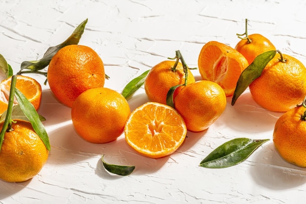 Mandarini (arance, mandarini, clementine, agrumi) con foglie verdi. Luce dura moderna, ombra scura. Sfondo di mastice bianco, disposizione piatta creativa, primo piano
