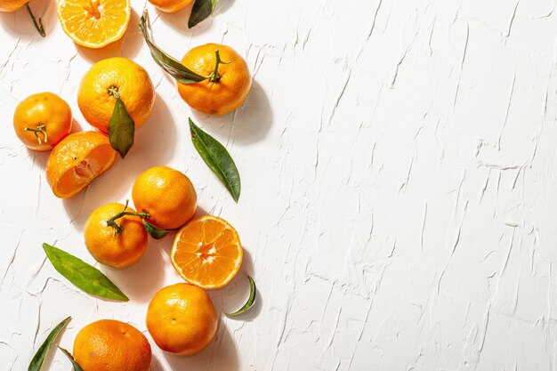 Mandarini (arance, mandarini, clementine, agrumi) con foglie verdi. Luce dura moderna, ombra scura. Sfondo di mastice bianco, disposizione piatta creativa, vista dall'alto