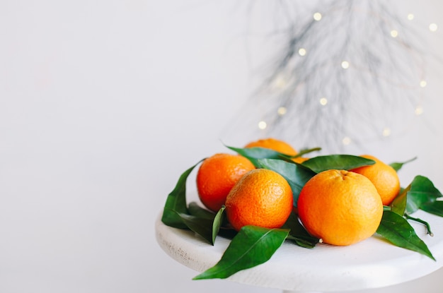 Mandarini arancioni su sfondo grigio nell'arredamento di Capodanno con pigne marroni e foglie verdi. Decorazione natalizia con mandarini. Deliziosa clementina dolce.