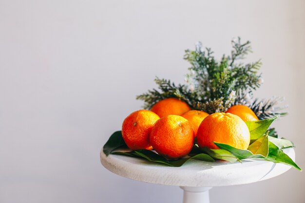 Mandarini arancioni su sfondo grigio nell'arredamento di Capodanno con pigne marroni e foglie verdi. Decorazione natalizia con mandarini. Deliziosa clementina dolce.