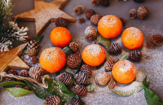 Mandarini arancioni su sfondo grigio nell'arredamento di Capodanno con pigne marroni e foglie verdi. Decorazione natalizia con mandarini. Deliziosa clementina dolce.