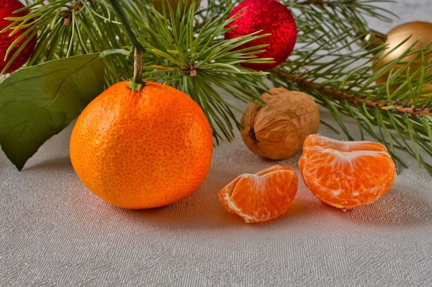 Mandarino e noce vicino al ramo di conifere. succose fette di mandarino sul tavolo vicino all'albero di Natale.