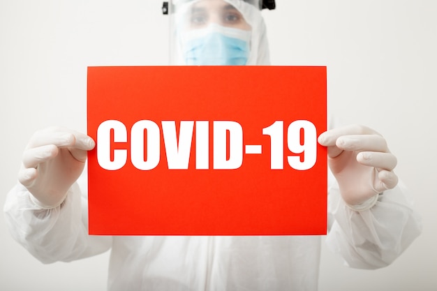 Mandi un sms a covid-19 su segnale di pericolo rosso in mani dei medici. Protezione dal coronavirus. Medico in tuta medica protettiva, rischio biologico, maschera su sfondo bianco. Concetto di assistenza sanitaria di laboratorio di medicina