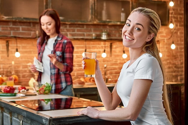 Mangia meno succo più giovane donna felice in piedi in una cucina moderna con un bicchiere di