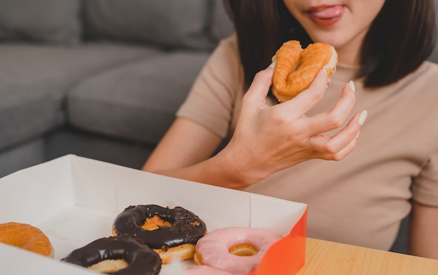 Mangiare ciambella quando da asporto e consegna. Fast food da asporto a casa. Stile di vita della donna asiatica in soggiorno. Distanziamento sociale e nuova normalità.