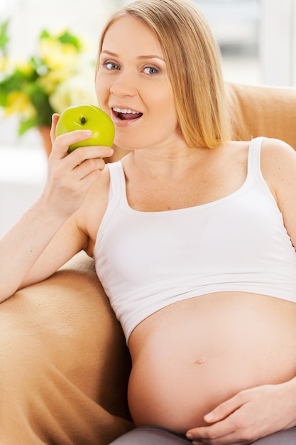 Mangiare fresco e sano. Bella donna incinta seduta sulla sedia e mangia mela verde