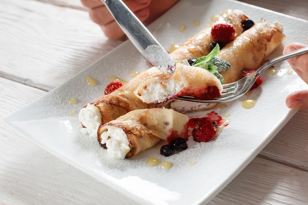 Mangiare frittelle con ricotta e frutti di bosco. Dessert fatto in casa di crepe con lamponi sul piatto bianco.