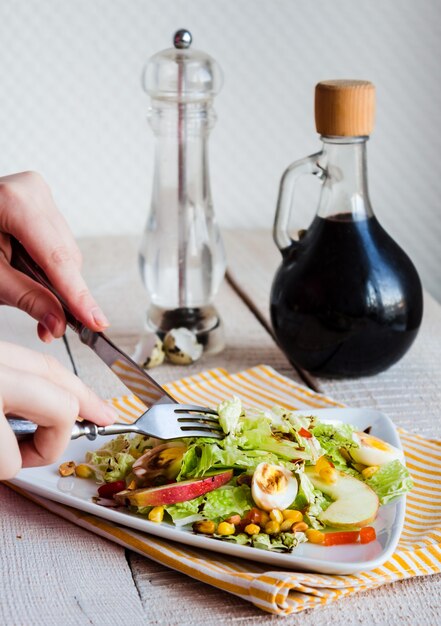 Mangiare insalata verde con uova di quaglia, mais e mela, mano, forchetta e coltello