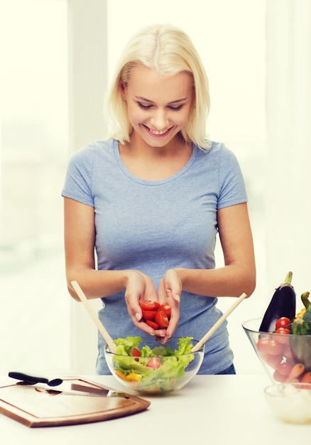 mangiare sano, cibo vegetariano, dieta e concetto di persone - giovane donna sorridente che cucina insalata di verdure a casa