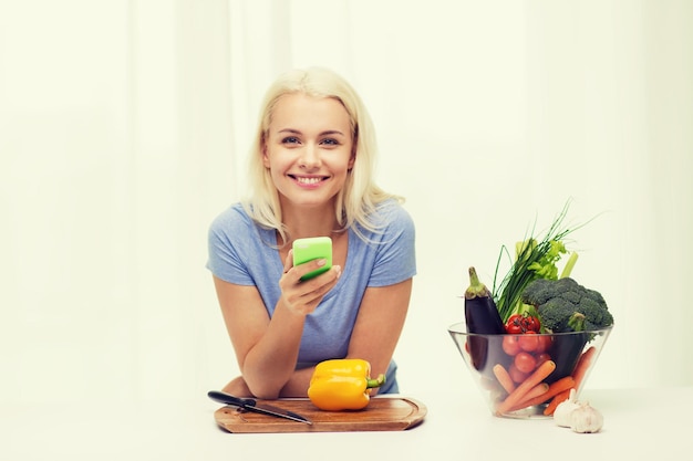 mangiare sano, cibo vegetariano, dieta e concetto di persone - giovane donna sorridente con smartphone che cucina le verdure a casa