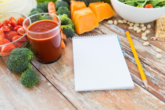 mangiare sano, cibo vegetariano, pubblicità e concetto culinario - primo piano di verdure mature e taccuino con matita su tavola di legno