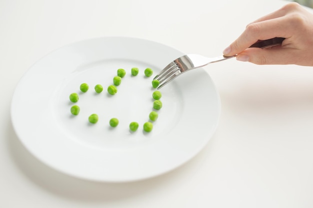 mangiare sano, dieta, cibo vegetariano e concetto di persone - primo piano di donna con forchetta che mangia piselli a forma di cuore