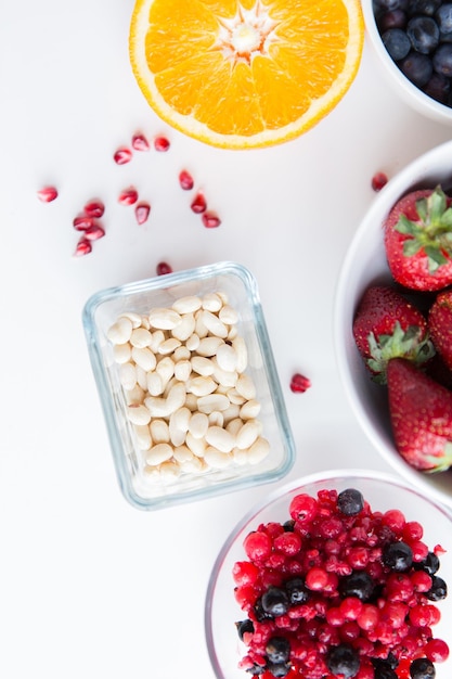 mangiare sano, dieta, cibo vegetariano e concetto di persone - primo piano di frutta, arachidi e bacche in ciotole sul tavolo