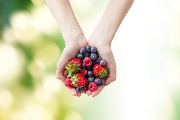 mangiare sano, dieta, cibo vegetariano e concetto di persone - primo piano di mani di donna che tengono diverse bacche estive mature su sfondo naturale verde