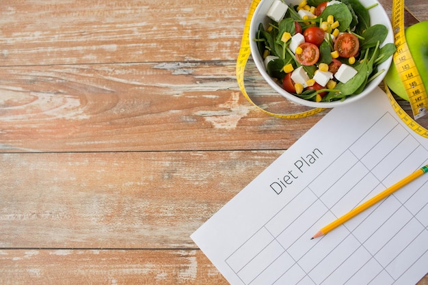 mangiare sano, dieta, dimagrimento e concetto di perdita di peso - primo piano della mela verde della carta del programma di dieta, nastro di misurazione e insalata