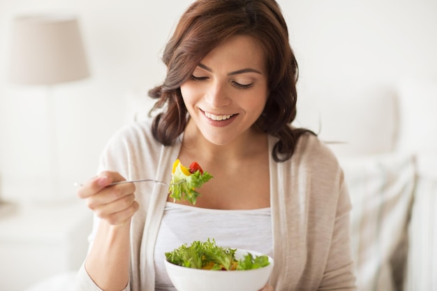 mangiare sano, dieta e concetto di persone - giovane donna sorridente che mangia insalata di verdure a casa