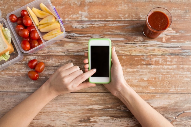 mangiare sano, dieta, tecnologia e concetto di persone - primo piano delle mani della donna con smartphone vuoto e cibo in contenitore di plastica sul tavolo a casa