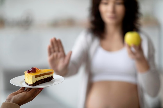 Mangiare sano durante la gravidanza Giovane donna incinta che rifiuta la torta e sceglie la mela