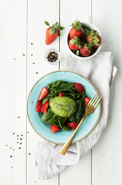 Mangiare sano. Insalata con fragole, avocado, spinaci su un fondo di legno bianco vista dall'alto laici piatta