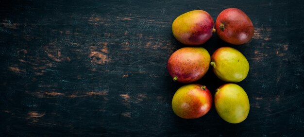 Mango con foglie su uno sfondo di legno nero Frutti tropicali Vista dall'alto spazio libero per il testo