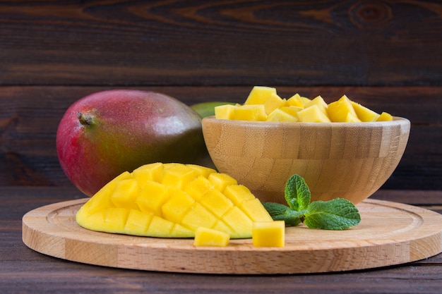Mango della frutta tropicale in un piatto su un fondo di legno, intero o affettato.