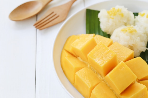 Mango e riso appiccicoso in piatto bianco sul pavimento di legno bianco.