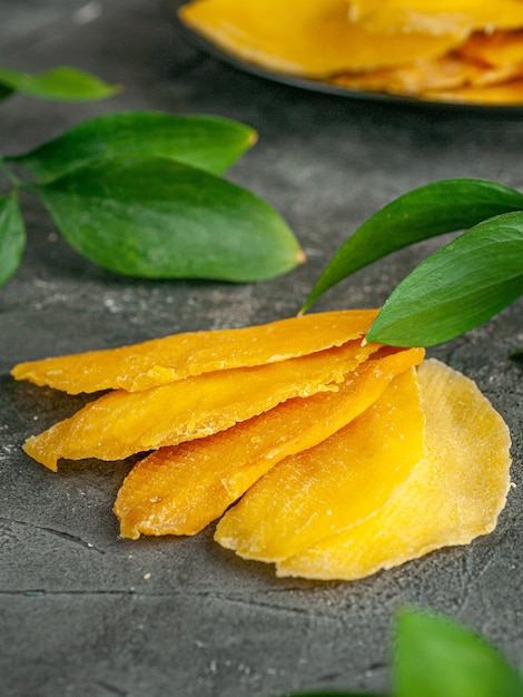 Mango essiccato affettato a fette su uno sfondo scuro. Nelle vicinanze ci sono rami di verde. Avvicinamento. macro