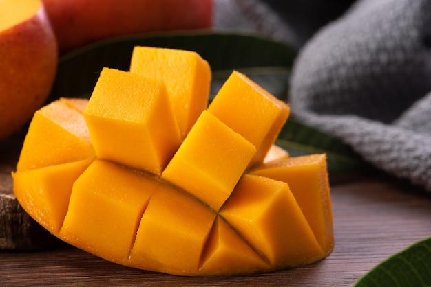 Mango. Primo piano di frutta fresca di mango maturo con foglie su sfondo tavolo in legno scuro con foglie verdi.