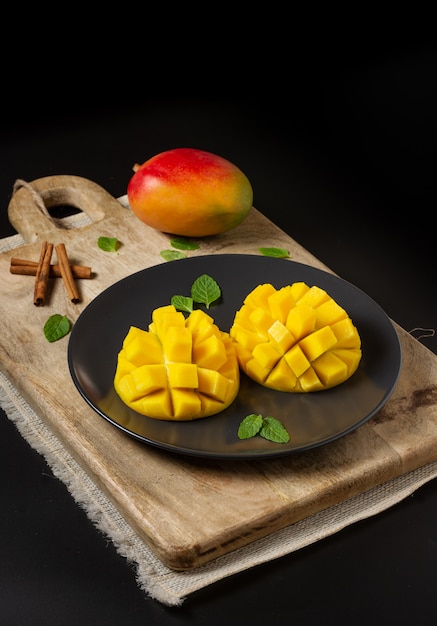 Mango tagliato a metà e tagliato a cubetti su una tavola di legno e mango intero, superficie nera con spazio per la copia