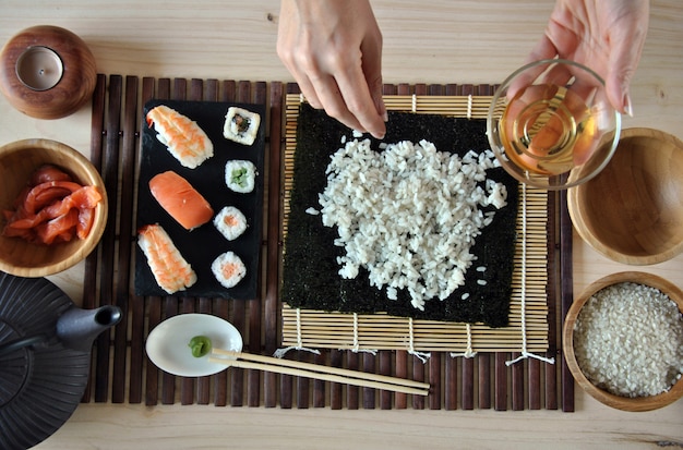 Mani che cucinano sushi con riso, salmone e nori