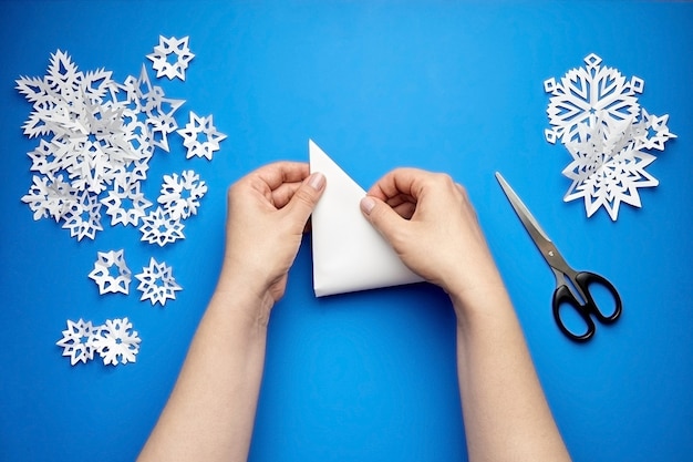 Mani che fanno i fiocchi di neve di carta bianca sull'azzurro