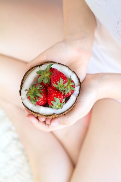 Mani che impilano fragole e uva nel guscio di noce di cocco