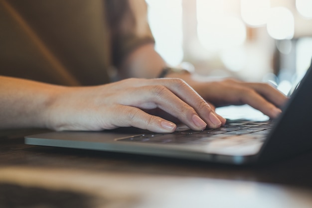 mani che lavorano e digitando sulla tastiera del computer portatile sul tavolo con sfocatura dello sfondo