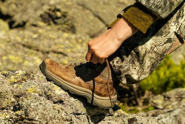 Mani che legano i lacci delle scarpe su un primo piano di uno scarpone da trekking consumato