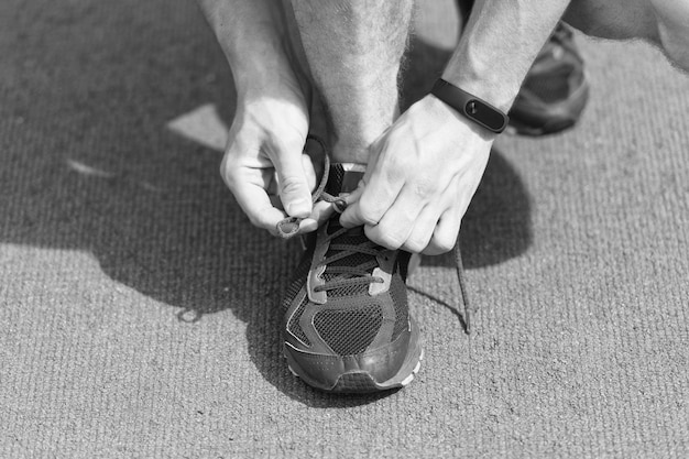 Mani che legano i lacci delle scarpe sullo sfondo della superficie da corsa della sneaker Mani di sportivo con pedometro che legano i lacci delle scarpe sulla sneaker sportiva Concetto di attrezzatura da corsa Legatura dei lacci da mani maschili