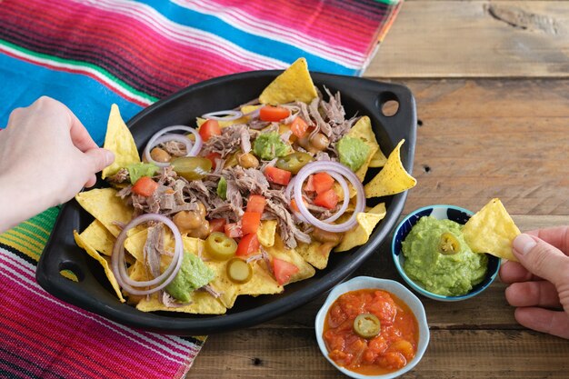 Mani che prendono il cibo da un vassoio di nachos con carne Ciotole con salsa Vista dall'alto Spazio di copia