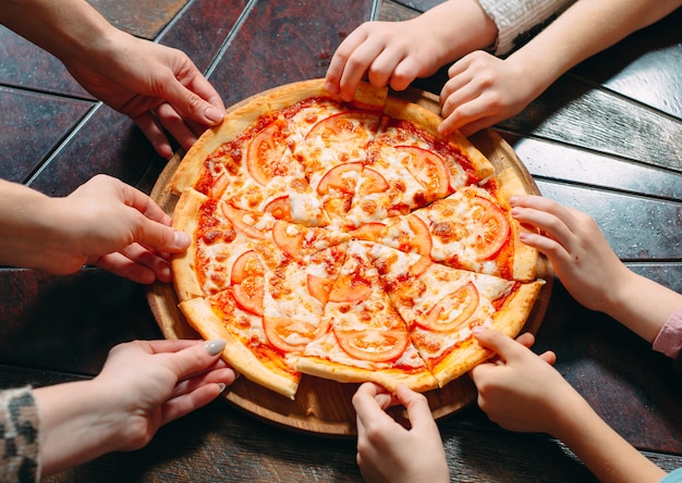 Mani che prendono le fette della pizza dalla tavola di legno, vista alta vicina.