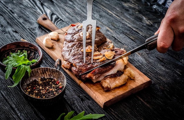 Mani che tagliano carne alla griglia con aglio su una tavola di legno